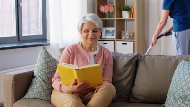 Anciana leyendo libro y ama de llaves en casa — Vídeos de Stock