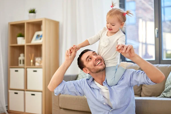 father riding little baby daughter on neck at home