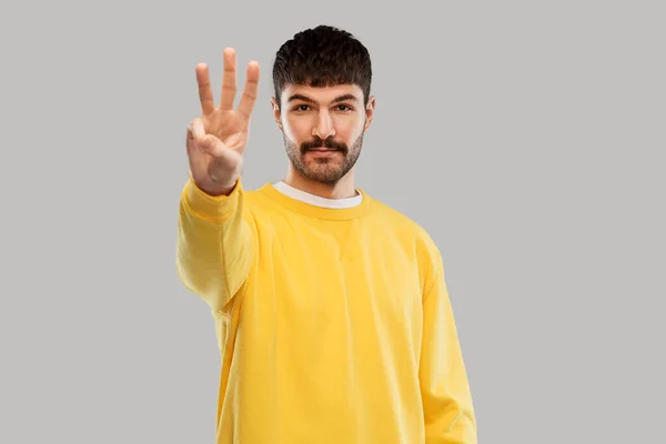 Mann in gelbem Sweatshirt zeigt drei Finger — Stockfoto