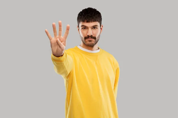 Hombre con sudadera amarilla mostrando cuatro dedos —  Fotos de Stock