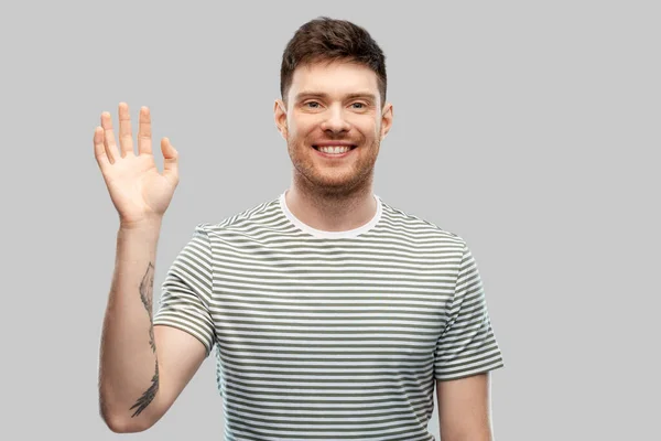 Lächelnder junger Mann im gestreiften T-Shirt winkt mit der Hand — Stockfoto