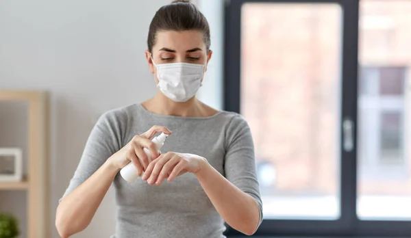 Close up of woman in mask spraying hand sanitizer — Stock Photo, Image