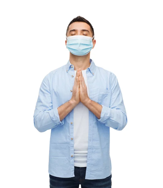 Молодой человек в защитной медицинской маске молится — стоковое фото