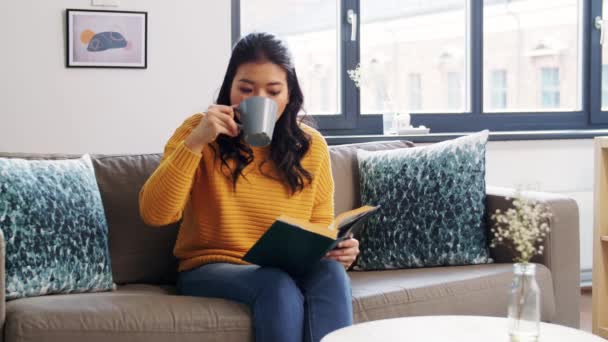 Asiatisk kvinna läser bok och dricker kaffe hemma — Stockvideo