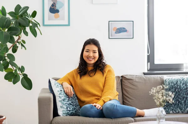 Mosolygós ázsiai fiatal nő ül kanapén otthon — Stock Fotó