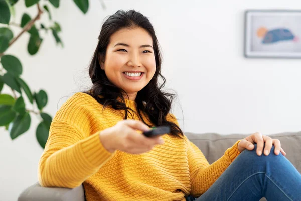 Mulher asiática com tv remoto sentado no sofá em casa — Fotografia de Stock