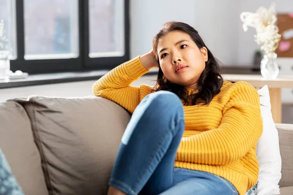 Worried asian young woman sitting on sofa at home — Stock Photo, Image