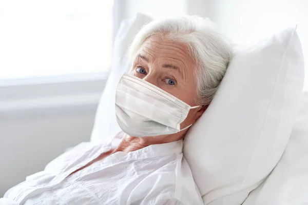 Starsza kobieta w masce leżąca w łóżku w szpitalu — Zdjęcie stockowe