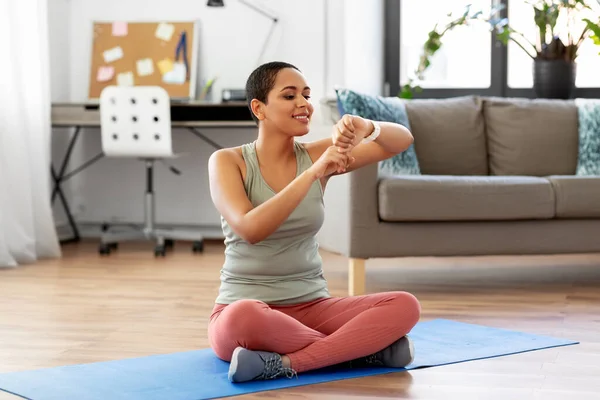 Mulher com relógio inteligente e tapete de exercício em casa — Fotografia de Stock