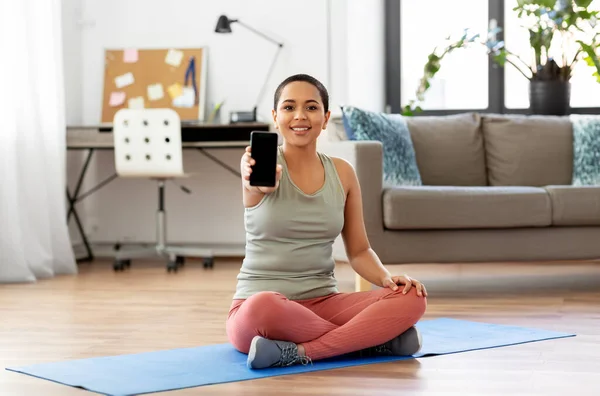 Žena s chytrým telefonem sedí na cvičení podložka doma — Stock fotografie