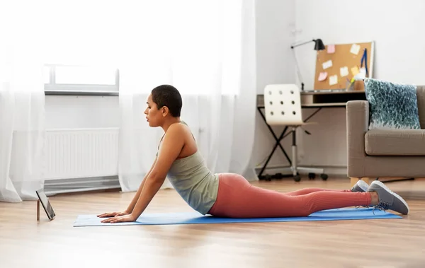 Mujer con tablet pc haciendo yoga cobra pose en casa — Foto de Stock