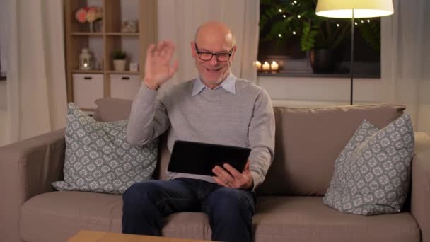 Старик с планшетным компьютером, имеющий видеозвонок дома — стоковое видео