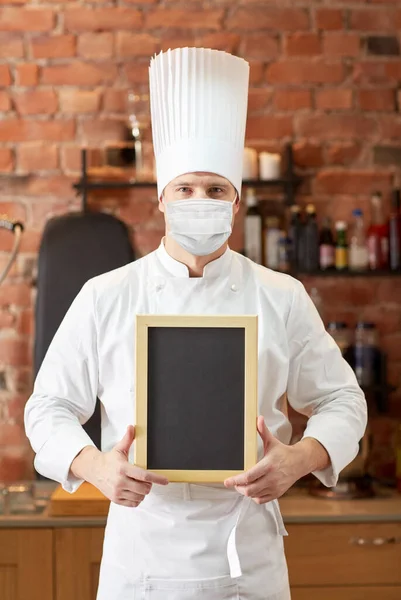 Male chef in face mask with black menu chalk board — Stock Photo, Image