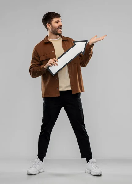 Smiling young man holding big white arrow — Stock Photo, Image