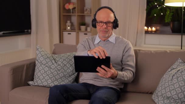 Senior man with tablet pc and headphones at home — Stock Video