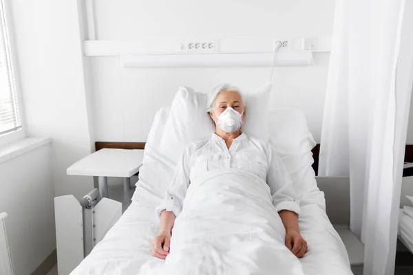 Mulher velha paciente em máscara deitada na cama no hospital — Fotografia de Stock