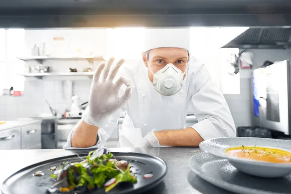 Chef macho em máscara com comida na cozinha do restaurante — Fotografia de Stock