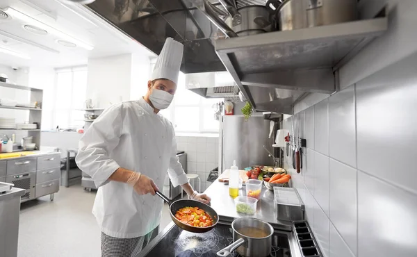 Koch in Maske kocht Essen in Restaurantküche — Stockfoto