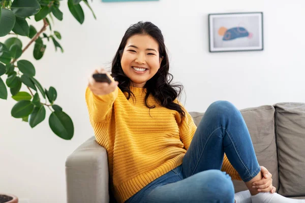 Mulher asiática com tv remoto sentado no sofá em casa — Fotografia de Stock