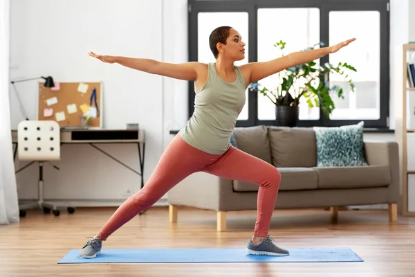 Mujer africana haciendo yoga guerrero pose en casa — Foto de Stock