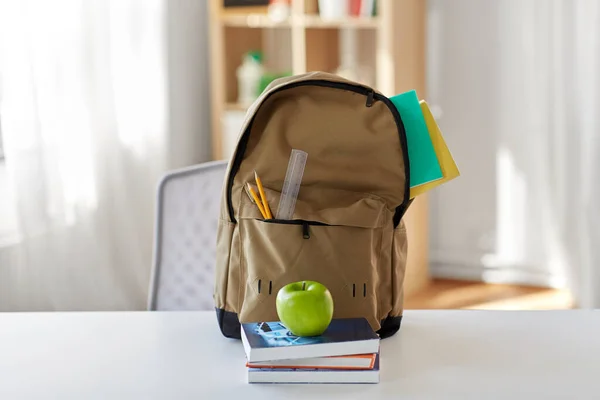 school backpack with books and apple on table