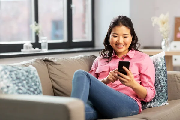 Feliz asiático jovem mulher com smartphone em casa — Fotografia de Stock