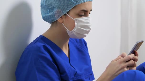 Doctor trist sau asistentă medicală în mască de față cu smartphone — Videoclip de stoc