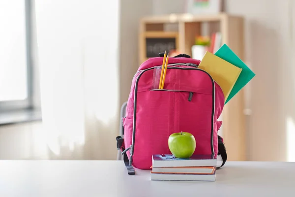 Rózsaszín hátizsák, alma és iskolai kellékek az asztalon — Stock Fotó