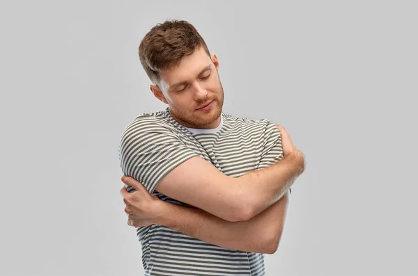 Щасливий молодий чоловік в смугастій футболці обіймає себе — стокове фото