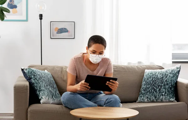 Žena v lékařské masce s tabletem PC doma — Stock fotografie