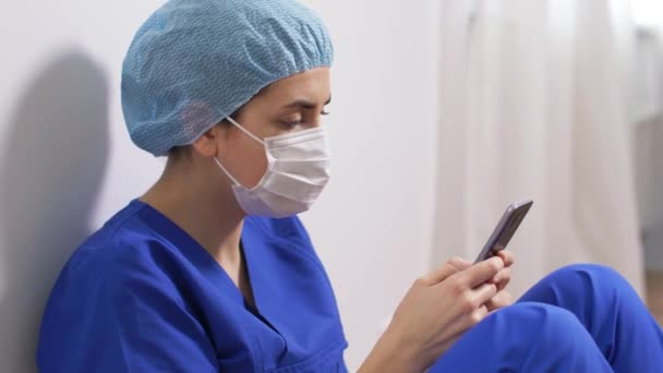 Грустный врач или медсестра в маске со смартфоном — стоковое видео