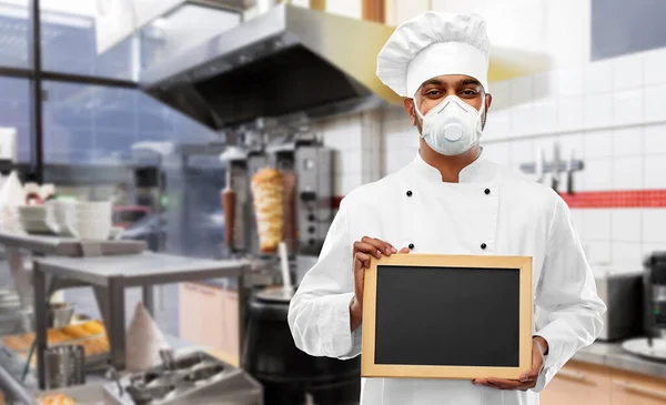 Chef in respirator with chalkboard at kitchen — Stock Photo, Image