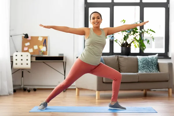 Mujer africana haciendo yoga guerrero pose en casa — Foto de Stock