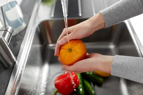 Kvinna tvätta frukt och grönsaker i köket — Stockfoto