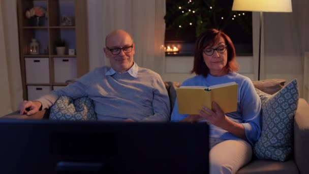 Casal sênior assistindo tv e livro de leitura em casa — Vídeo de Stock