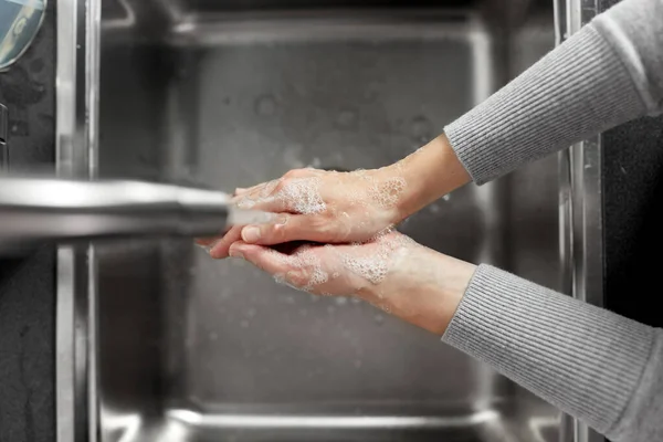 Mujer lavándose las manos con jabón en la cocina — Foto de Stock