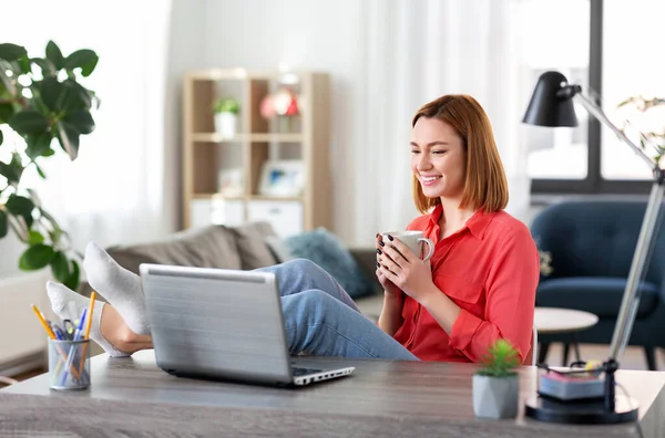 Γυναίκα με φορητό υπολογιστή πίνοντας καφέ στο γραφείο στο σπίτι — Φωτογραφία Αρχείου