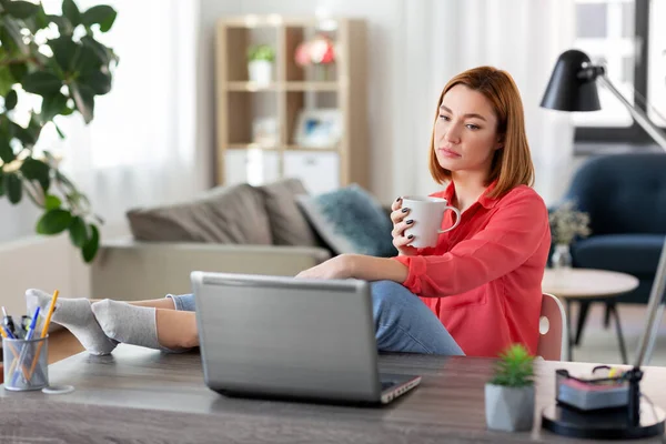 Γυναίκα με φορητό υπολογιστή πίνοντας καφέ στο γραφείο στο σπίτι — Φωτογραφία Αρχείου