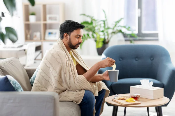 Хворий молодий чоловік у ковдрі п'є гарячий чай вдома — стокове фото