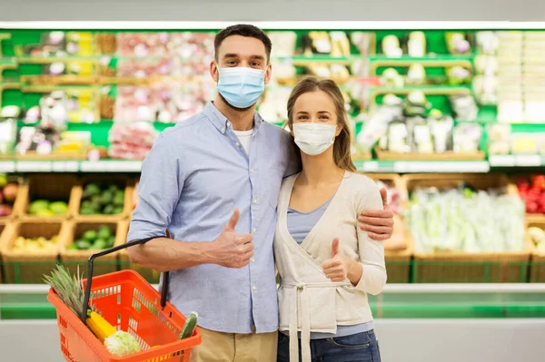 Pareja en máscaras con cesta de comida en la tienda de comestibles — Foto de Stock