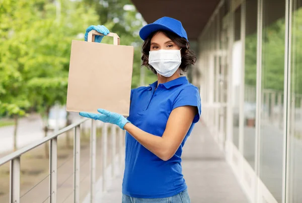 Levering vrouw in gezicht masker met voedsel in papieren zak — Stockfoto