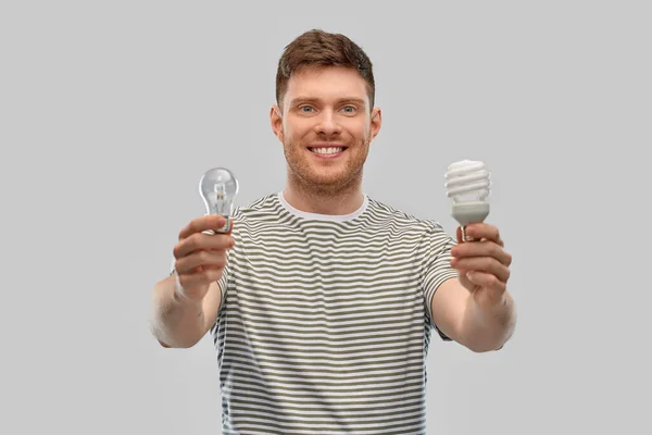 Smiling young man comparing different light bulbs — Stock Photo, Image