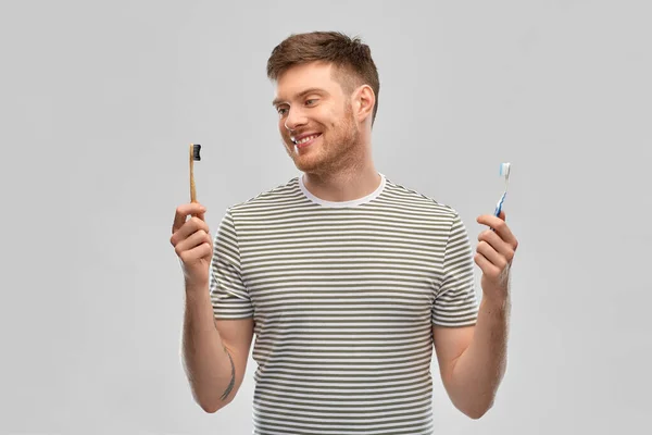 Hombre que compara el cepillo de dientes de madera y plástico — Foto de Stock