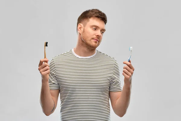 Человек сравнивает деревянную и пластиковую зубную щетку — стоковое фото