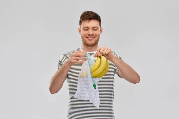 Улыбающийся человек кладет бананы в многоразовую сетку — стоковое фото