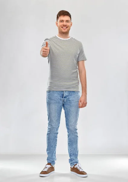 Nuori mies raidallinen t-paita näyttää peukalot ylös — kuvapankkivalokuva
