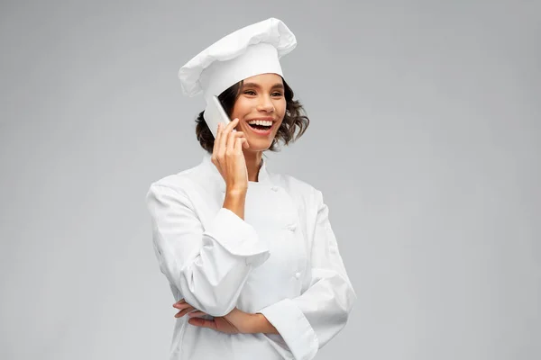 Улыбающаяся шеф-повар в токе звонит на смартфон — стоковое фото