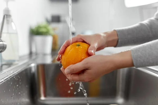 Close up de mulher lavando frutas laranja na cozinha — Fotografia de Stock