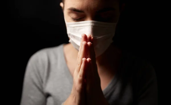 Chora młoda kobieta w masce ochronnej modląca się — Zdjęcie stockowe