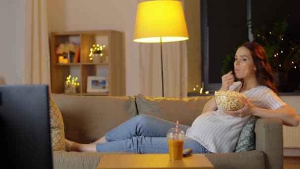 Беременная женщина с попкорном смотрит телевизор дома — стоковое видео
